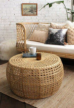 Load image into Gallery viewer, Rattan coffee table, wicker ottoman, rattan end table. Round caned coffee table ottoman end table in front of wicker daybed. Styled in cool tones against a painted brick wall.
